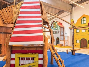 A play structure with a red and white striped roof, wooden climbing elements, and a yellow door with a window. - Holiday Home in Wendtorf (Wendtorf)