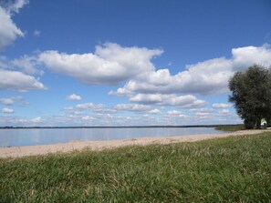 Escape to a serene lakeside haven with a tranquil grassy area leading to a sandy beach.