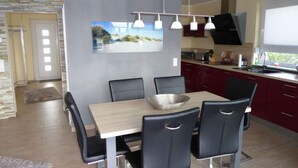 Egy modern étkező, melyben egy fa asztal és fekete székek találhatók, egy piros szekrényekkel berendezett konyha, és egy nagy ablak.