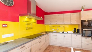 Una cocina con paredes amarillas y rojas, una campana extractora de acero inoxidable, un microondas y un lavabo.