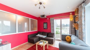 Una sala de estar moderna con una pared destacada en rojo, un sofá gris, un tapete rojo y un ventanal con vistas al exterior.