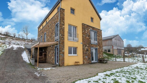 Un edificio amarillo de dos pisos con detalles de piedra, un porche cubierto y un camino de entrada de grava.