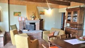 A cozy living room with a fireplace, comfortable seating, and a wooden dining table. - Belvilla by OYO Ciliegi (Cortona)