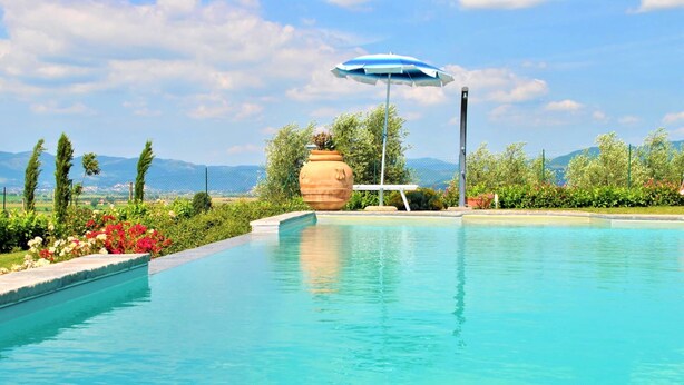 A swimming pool with a clear view of the surrounding landscape, including trees and distant mountains. - Belvilla by OYO Ciliegi (Cortona)