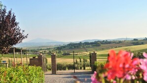 A rural landscape with a gated entrance, a gravel path, and a view of rolling hills and fields. - Belvilla by OYO Ciliegi (Cortona)