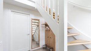 Un interior moderno con una puerta blanca, una escalera de madera y un perchero metálico.
