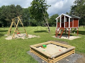 A playground with a swing set, a sandpit, and a wooden playhouse.