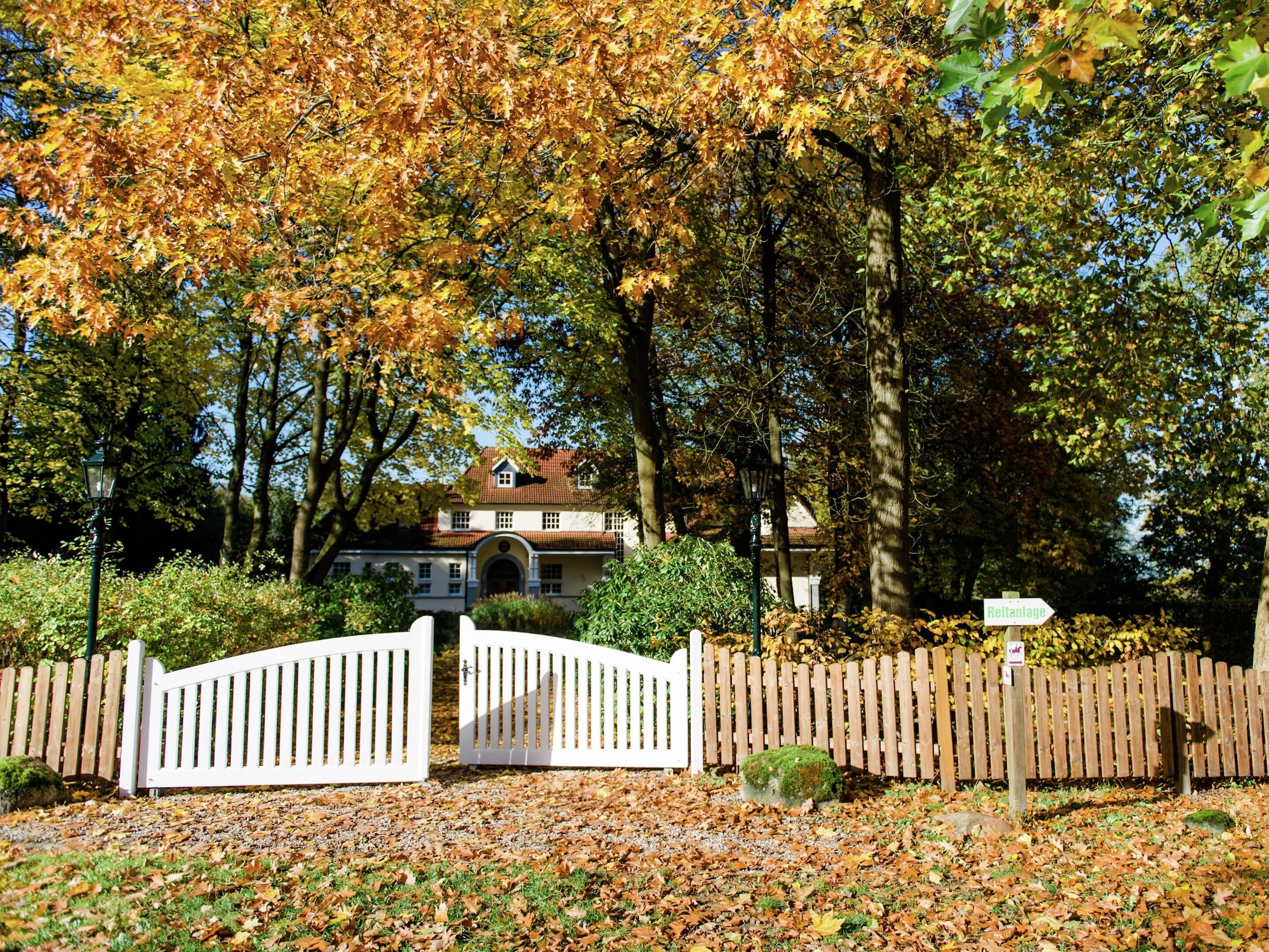 A gated entrance to a house with a red-tiled roof, surrounded by trees with autumn leaves.