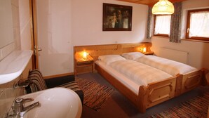 Una habitación con cama de madera, una mesita de noche, un cuadro en la pared y una ventana con cortinas.