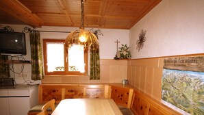 Una mesa de madera para comer con bancos, un televisor sobre un mueble bajo y una ventana con cortinas.