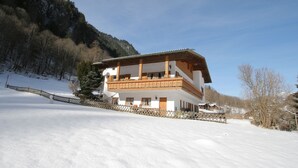 Un chalet de dos pisos con un balcón, rodeado de nieve y árboles.