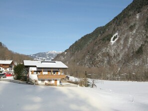 Un edificio in stile chalet con tetto spiovente, circondato da terreno innevato e montagne boscose sullo sfondo.