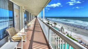 A balcony with a view of the beach, lounge chairs, and a lifeguard stand. - Oceanfront Condo w/ Largest Balcony & Beach Access (Daytona Beach)
