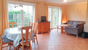 Un coin repas avec une table ronde et des chaises, un meuble en bois avec un téléviseur, et un canapé dans un salon doté de grandes fenêtres.