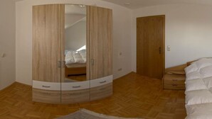 A bedroom with a wooden wardrobe, a bed, and a herringbone-patterned floor. - Liefde Voor de Eifel (Huertgenwald)