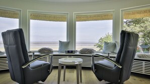 A room with two black leather chairs facing a large window overlooking a beach. There is a small round table in the center. - House by the sea Comfortable Holiday Residence (Sylt)