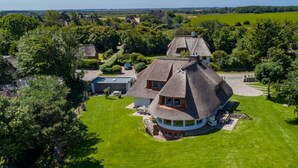 A large, circular house with a thatched roof, surrounded by a well-maintained lawn and trees. - House by the sea Comfortable Holiday Residence (Sylt)