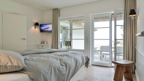 A bedroom with a bed, a TV, a bedside table, and a view of the outdoor patio. - House by the sea Comfortable Holiday Residence (Sylt)