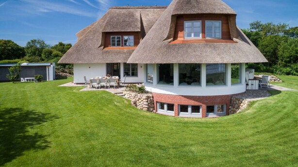 A house with a thatched roof and a circular section with large windows. - House by the sea Comfortable Holiday Residence (Sylt)