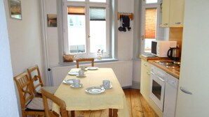 Une petite cuisine avec une table à manger pour quatre personnes, des chaises en bois, un four à micro-ondes, une cuisinière et une fenêtre avec des stores.