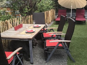 A patio with a wooden table set for four, surrounded by wicker chairs with red cushions. - Holiday Home Lower Lake Terrace (Rieden)