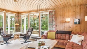 Un salón acogedor con techo de madera, ventanas amplias, un sofá, una mesa de centro y dos sillones.