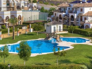 Una zona residencial con piscina, un pequeño puente y un edificio blanco con balcón.