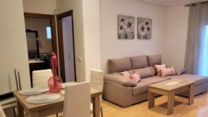 A modern living room with a beige sofa, a dining table with chairs, and a pink vase. - Apartment in Spain Near Sandy Beach (Vera)