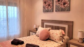 A bedroom with a bed, two nightstands, a window with curtains, and two floral paintings on the wall. - Apartment in Spain Near Sandy Beach (Vera)