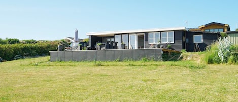 A modern house with a large deck, a garage, and a fenced yard.