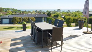 An outdoor deck with a dining table and chairs, surrounded by greenery and overlooking a residential area. - 4 Person Holiday Home in Slagelse (Slagelse)