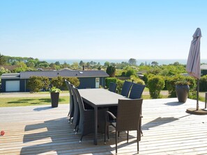 An outdoor deck with a dining table and chairs, surrounded by greenery and overlooking a residential area. - 4 Person Holiday Home in Slagelse (Slagelse)