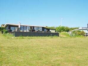A modern house with a large glass window area, a covered outdoor seating area, and a well-maintained lawn.