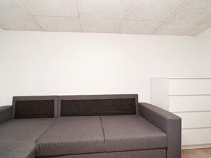 A grey sofa with two cushions against a plain white wall and a white cabinet. - 4 Person Holiday Home in Slagelse (Slagelse)