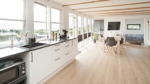 A modern kitchen with large windows, a dining area with a table and chairs, and a television mounted on the wall. - 4 Person Holiday Home in Slagelse (Slagelse)