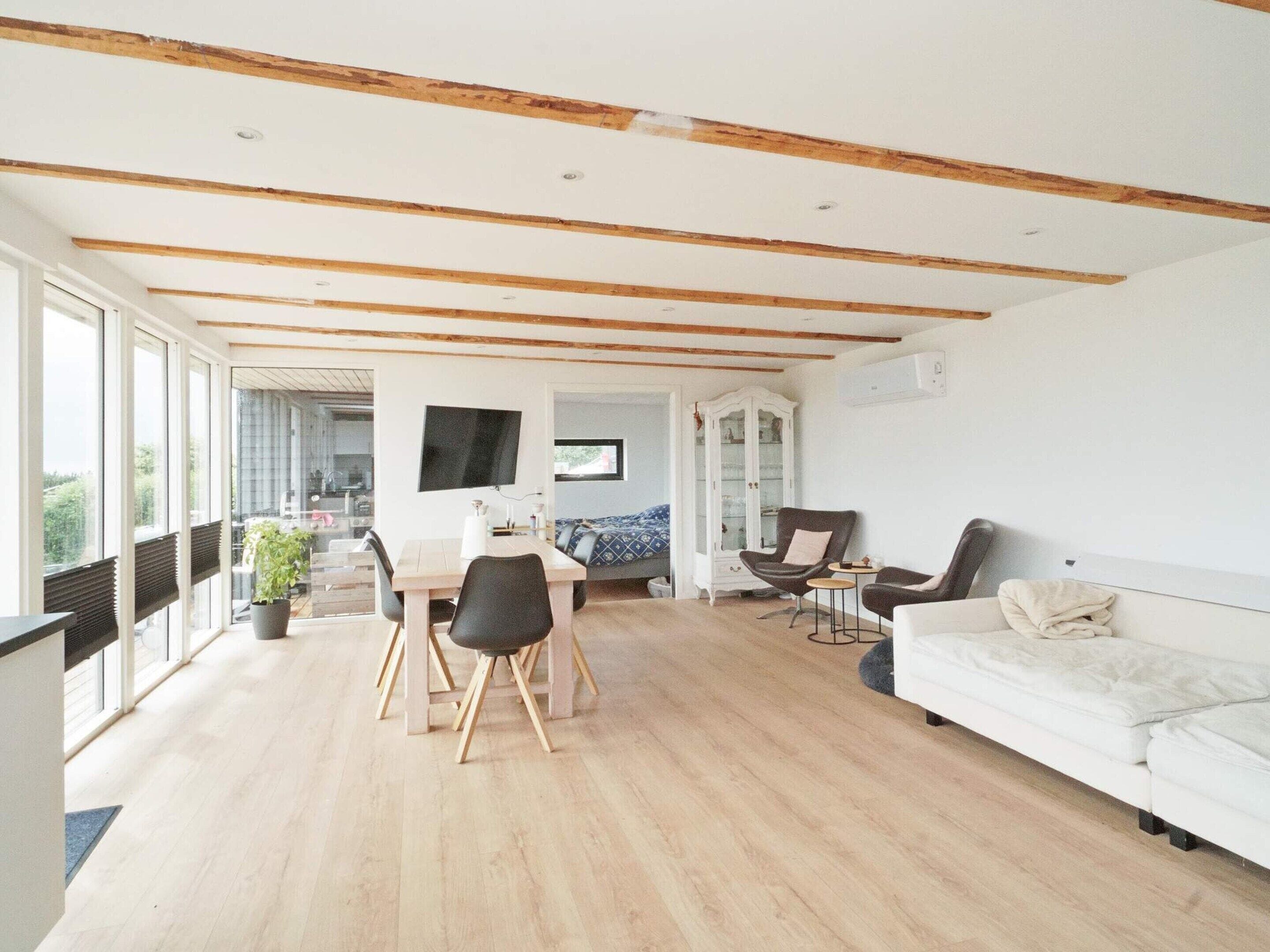 Amplia sala de estar con techo de madera, una mesa de comedor con sillas, un sofá y un televisor montado en la pared.