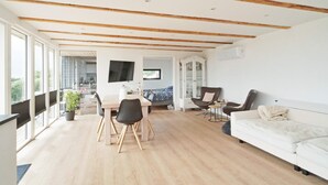 A spacious living area with a wooden ceiling, a dining table with chairs, a sofa, and a television mounted on the wall. - 4 Person Holiday Home in Slagelse (Slagelse)