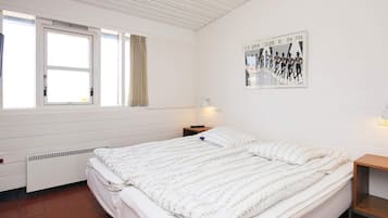 A bedroom with a bed, a window with curtains, a radiator, a wall-mounted picture, and a bedside table with a lamp.