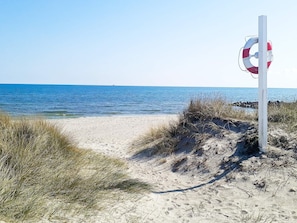 Une plage avec une bouée de sauvetage fixée à un poteau, une eau d’un bleu limpide et des dunes de sable.