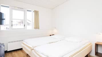 Una habitación con dos camas, una ventana, un calentador y una pequeña mesa.