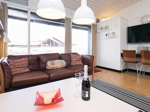 Een moderne woonkamer met een bruine leren bank, een witte tafel met een fles en glazen, en een groot raam met uitzicht op een gebouw.