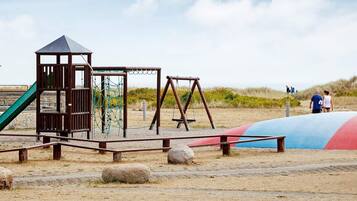 Un parque infantil con una estructura para escalar, columpios y un tobogán.