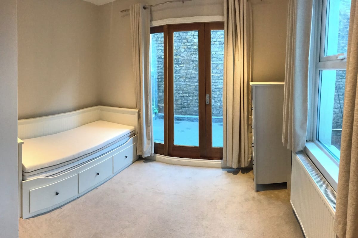 Une chambre d’angle avec un banc intégré, un radiateur et une vue à travers une porte vitrée.