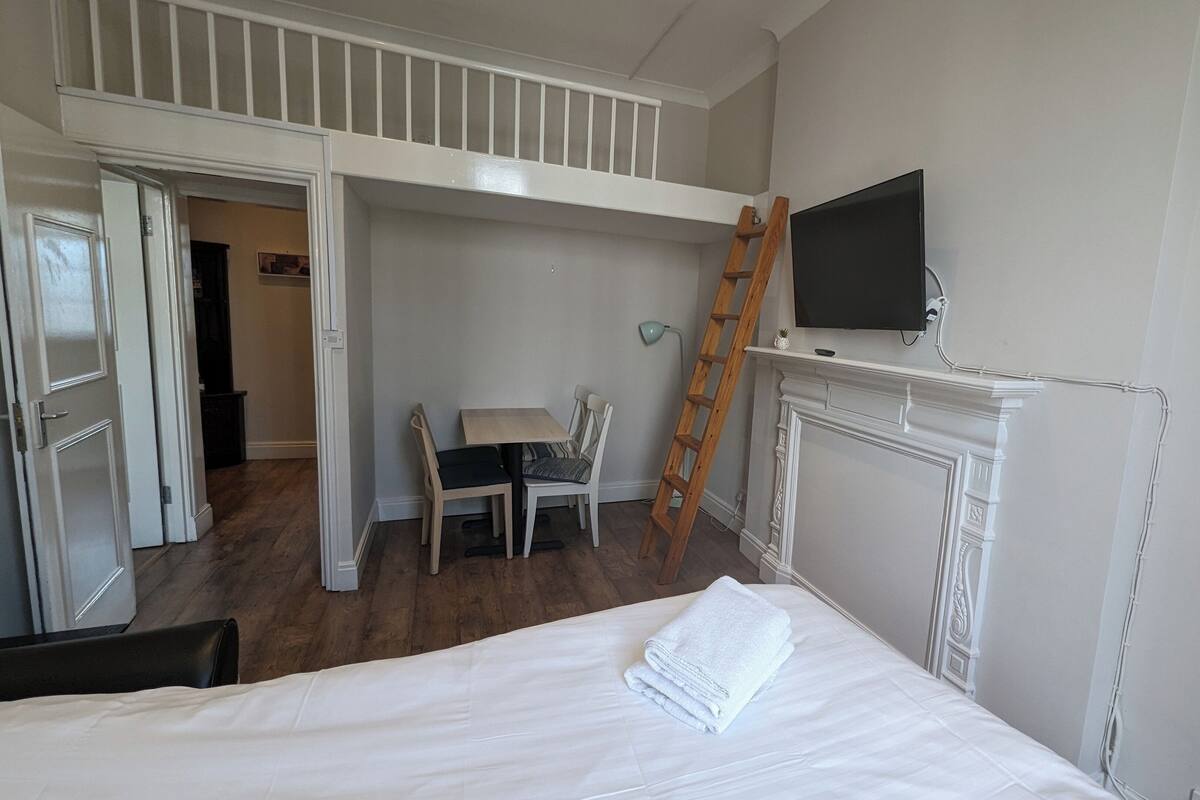Une chambre avec un lit en mezzanine, un bureau et un téléviseur fixé au mur.