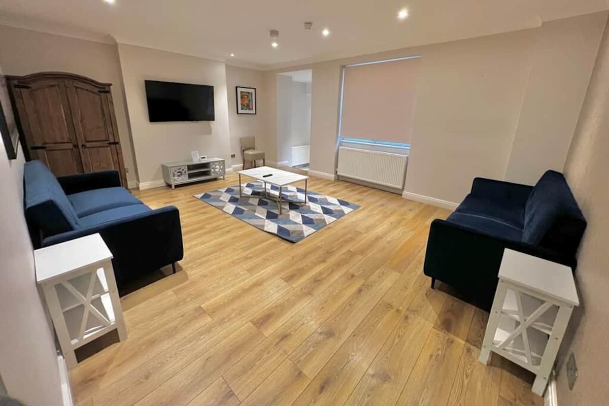 Un salon moderne avec deux canapés sombres, une table basse et un téléviseur fixé au mur.