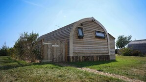 Un petit bâtiment en bois, doté d’un toit en pente et de deux fenêtres, entouré d’herbe et d’arbres.