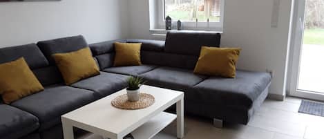 A modern living room with a grey sectional sofa, a white coffee table, and a window with a view of the outdoors.
