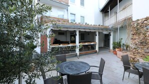 Un patio al aire libre con una mesa redonda y sillas, un área de estar cubierta con barandilla y una pared de piedra.
