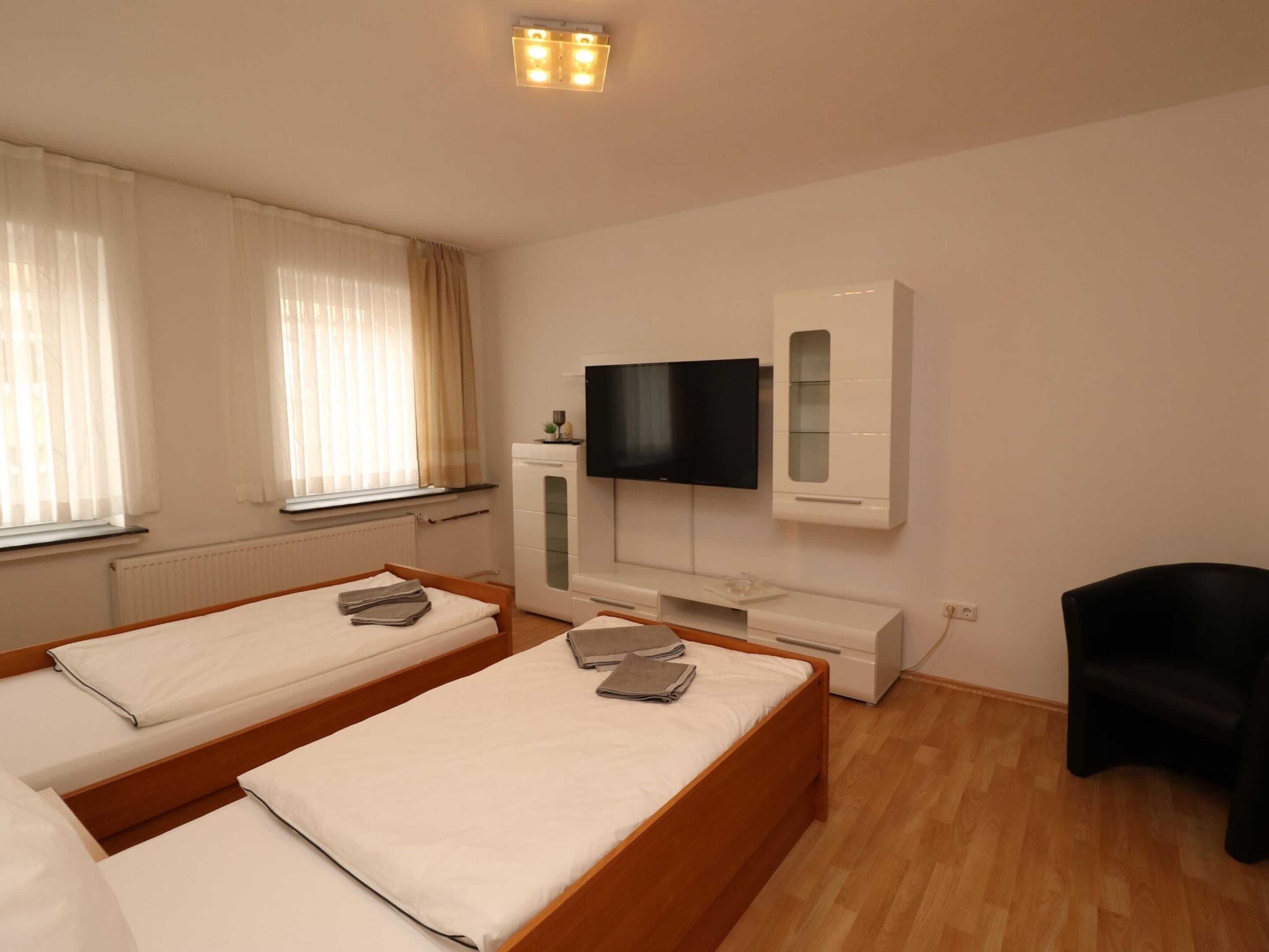 A hotel room with two beds, a TV, a small cabinet, and a chair.