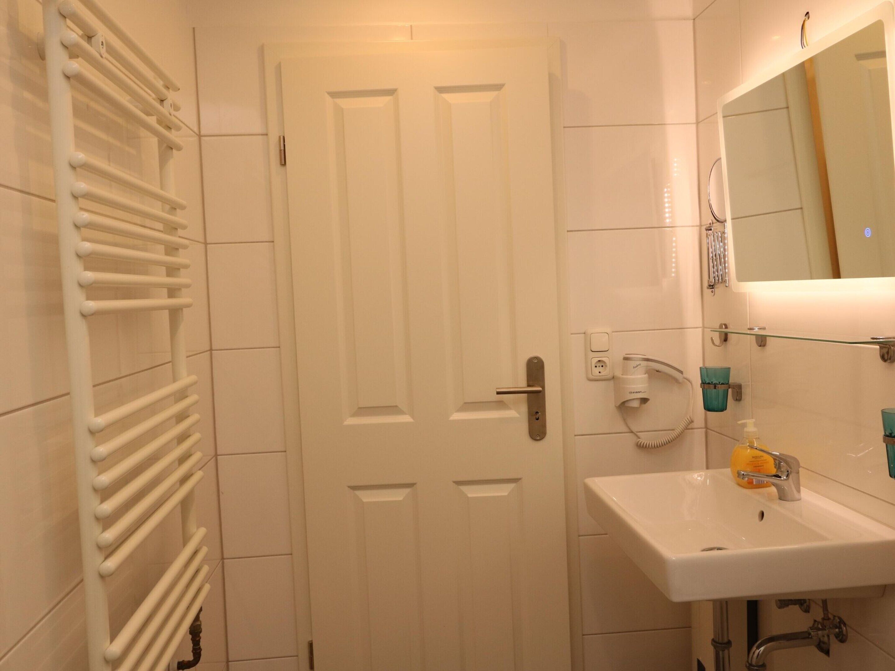 A bathroom with a white door, a white sink with a mirror, and a towel rack.